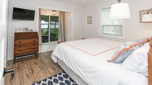 Une chambre à coucher comprenant un lit, une commode, un ventilateur de plafond, un téléviseur et une fenêtre avec des stores.