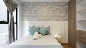 Une chambre à coucher bien rangée, avec un lit, des oreillers, une table de chevet et une armoire.