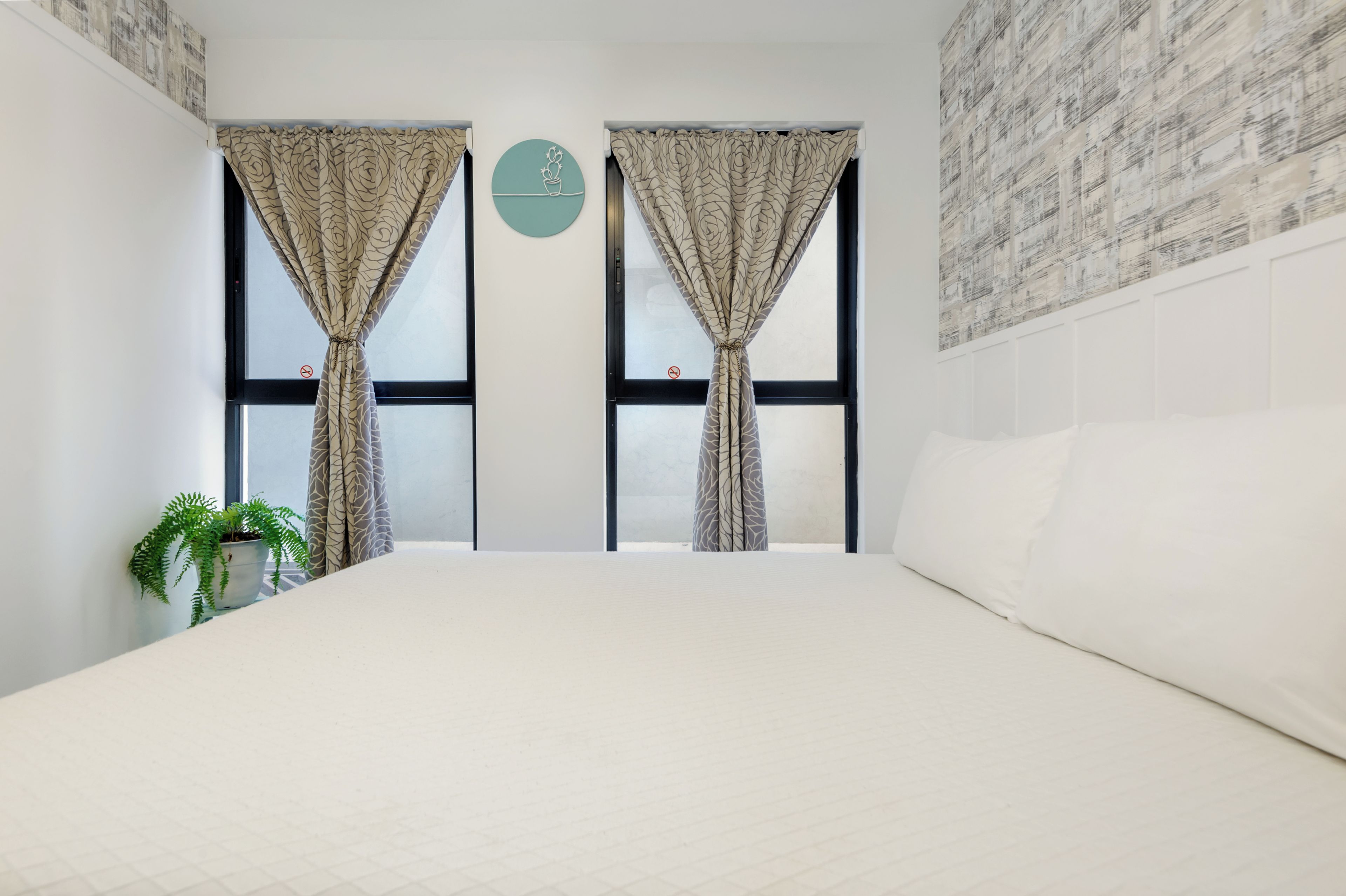 Een slaapkamer met een groot bed, twee ramen met gordijnen met een patroon, een kamerplant en een muur met een reliëfprint.
