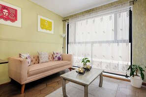 A living room with a sofa, a coffee table, and a window with sheer curtains.