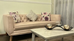Un salon avec un canapé beige, deux coussins à motifs, une table basse en bois agrémentée d’objets décoratifs, un sol à motifs hexagonaux et une fenêtre ornée de rideaux légers.