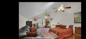 Une chambre avec un grand lit, un canapé en cuir, un bureau et une chaise. On y trouve également des ventilateurs de plafond et un tableau accroché au mur.