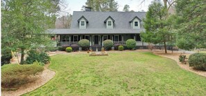 Stunning two-story house with a central entrance and flanked windows, set amidst a serene and lawn with mature trees.