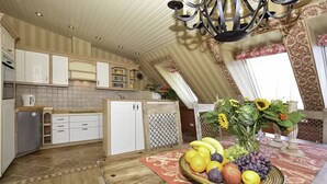 A kitchen with white cabinets, a wooden table with a fruit bowl, and a chandelier. - Ferienwohnung Meerblick - Penthouse, Dachterrasse, Meerblick, Strand (Binz)