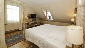 A bedroom with a large bed, a desk with a television, a window with curtains, and a lamp. - Ferienwohnung Meerblick - Penthouse, Dachterrasse, Meerblick, Strand (Binz)