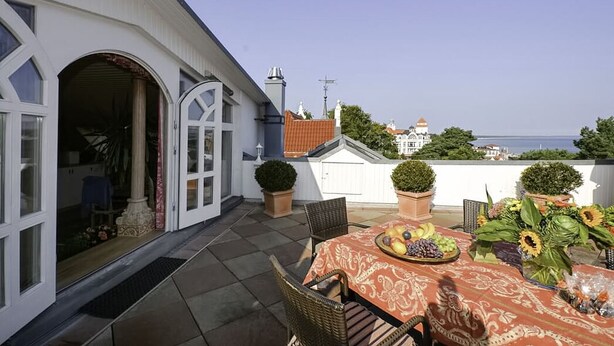 A terrace with a table set for dining, potted plants, and a view of the sea. - Ferienwohnung Meerblick - Penthouse, Dachterrasse, Meerblick, Strand (Binz)
