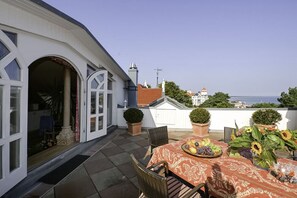 Una terraza con mesa lista para comer, plantas en macetas y vista al mar.