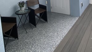 Een kamer met een blauwe muur, een bord met een welkomstboodschap, een deur met het getal '2', een klein tafeltje met een plant en twee stoelen.