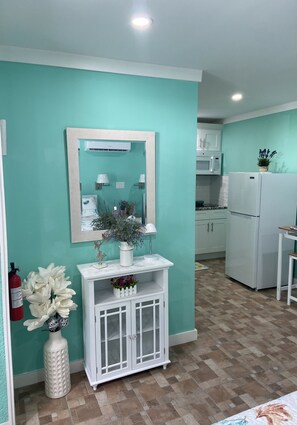 Una cocina con paredes verde azulado, armarios blancos y un refrigerador blanco.