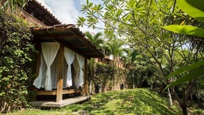 A covered outdoor seating area with white curtains, surrounded by lush greenery and a clear sky. - Casa Sunzal Boutique Hotel (Tamanique)