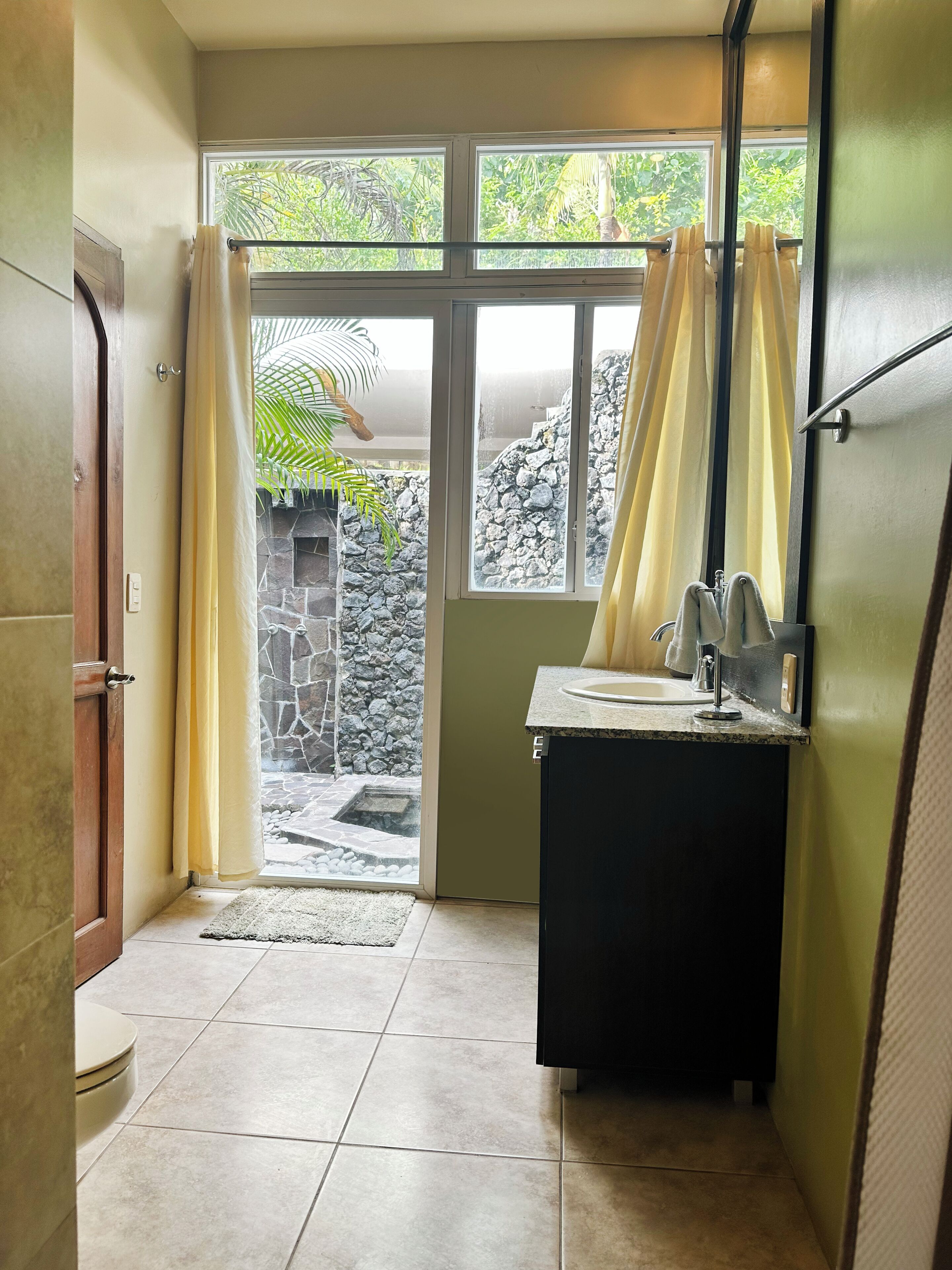 Casa de banho com lavatório, espelho e janela com cortinas.