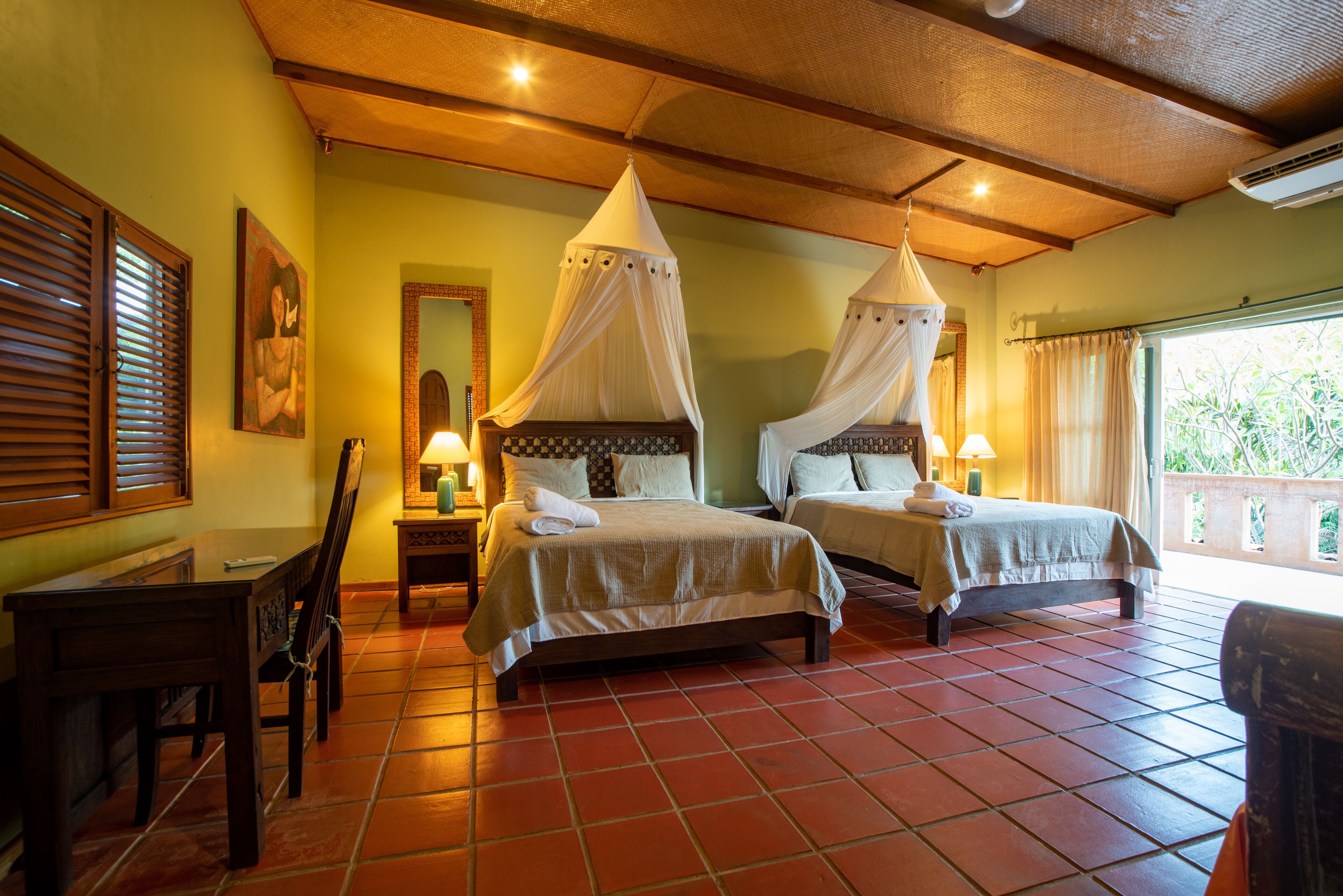 A room with two beds, each with a canopy, a wooden table, and a chair.