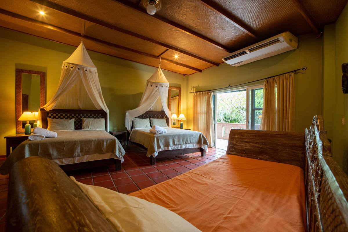 A bedroom with two beds, a large window with curtains, and an air conditioning unit.