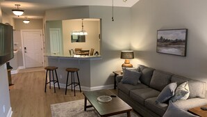A modern living room with a grey sofa, a coffee table, and a dining area with a kitchen counter.