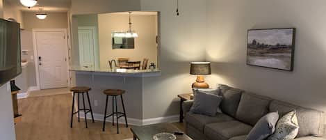 Una sala de estar moderna con un sofá gris, una mesa de centro y un comedor con una encimera de cocina.