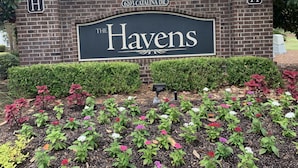 A sign for 'The Havens' at 6203 Catalina Dr., featuring a brick wall and a landscaped flower bed with various flowers.