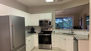 A modern kitchen with white cabinets, stainless steel appliances, a large window, and a view of the outdoors.