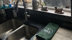 Eine Küche mit einem großen Spülbecken, einem Fenster mit Seeblick und einem Grill draußen.