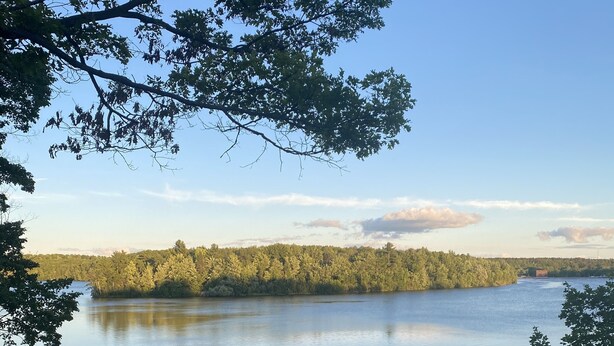 Eine Holzterrasse mit Blick auf einen ruhigen See und bewaldete Hügel in der Ferne.