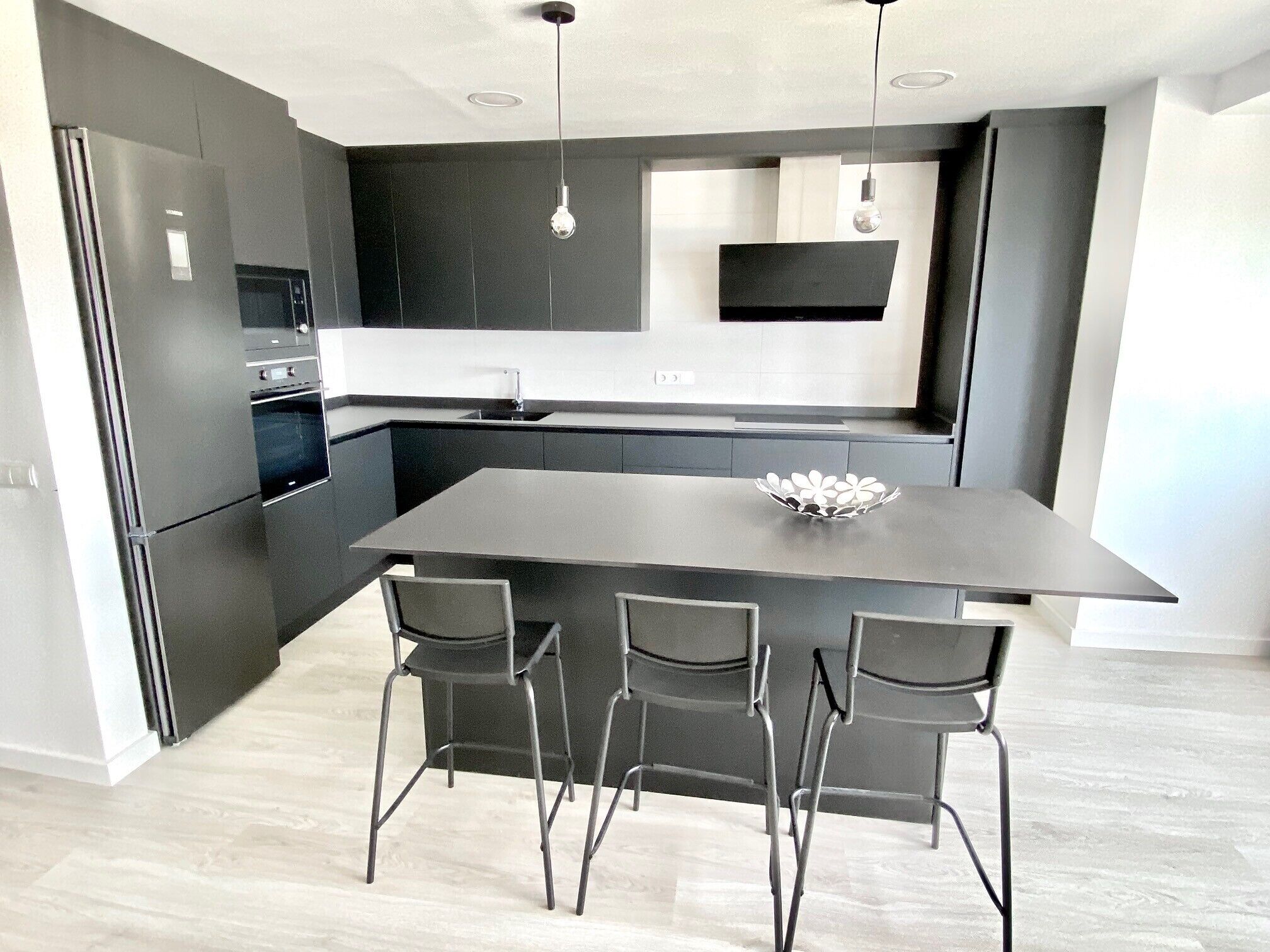 A modern kitchen with a central island, bar stools, and a built-in oven.