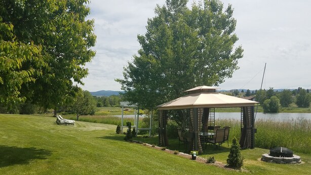 A gazebo with a table and chairs, surrounded by a grassy area and trees, near a body of water. - Montana Mountain Memories- RV in Orchard by Trout Pond (Florence)