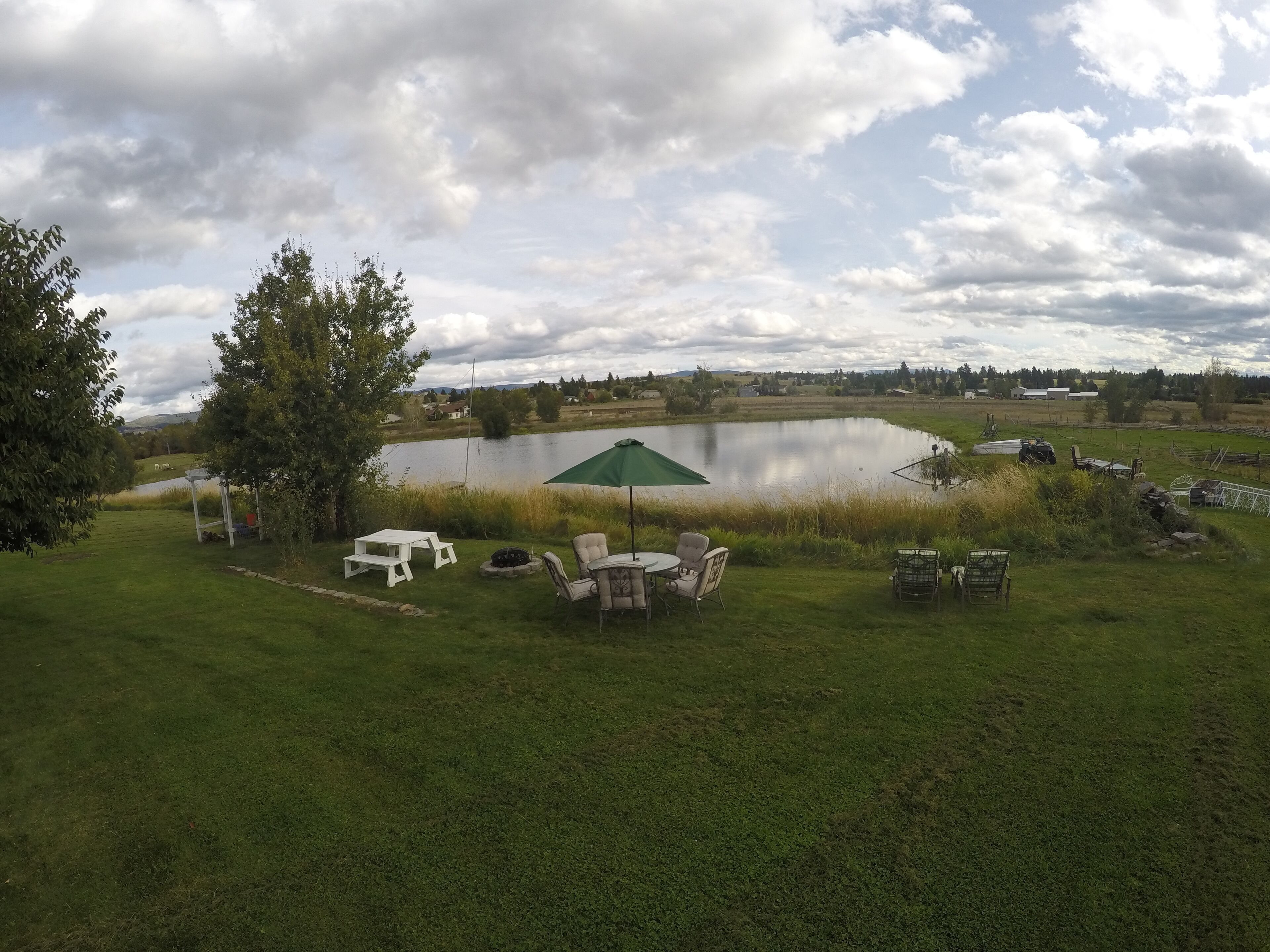 A lakeside outdoor area with picnic tables, chairs, and a green umbrella.