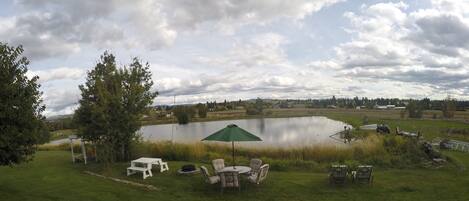A lakeside outdoor area with picnic tables, chairs, and a green umbrella.