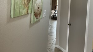 Un corridoio con due opere d'arte appese al muro, una porta e un pavimento piastrellato che conduce a una zona pranzo.