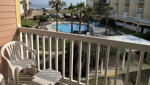 Un balcone con sedie bianche, una piscina, palme e vista sull'oceano e sugli edifici.