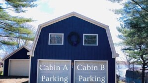 A blue cabin with two garage doors labeled 'Cabin A Parking' and 'Cabin B Parking.' - Lake Side Guest Suite (Hermon)