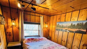 A wooden cabin room with a bed, a window, and wall-mounted lights. - Lake Side Guest Suite (Hermon)
