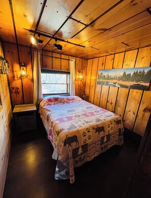 A wooden cabin room with a bed, a window, and wall-mounted lights.