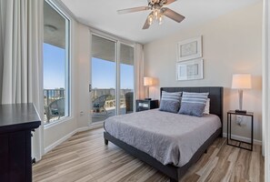 Une chambre avec un grand lit, un ventilateur de plafond, une vue sur la ville et un balcon.