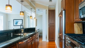 A modern kitchen with wooden cabinets, a black countertop, stainless steel appliances, and pendant lighting. - Waterfront 2BD Next to Pike Place w/ Private Patio (Seattle)