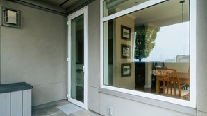 A modern room with a sliding glass door leading to a balcony, a small seating area with a table and chairs, and a wall-mounted air conditioning unit. - Waterfront 2BD Next to Pike Place w/ Private Patio (Seattle)
