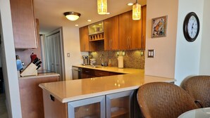 Een moderne keuken met houten kastjes, een centraal eiland en een eethoek met rieten stoelen.