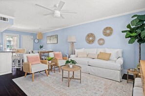 A living room with a white sofa, two armchairs, a coffee table, and a dining area with a table and chairs.