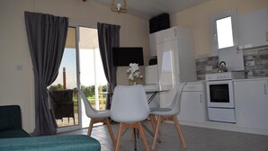 Een compacte keuken met witte apparaten, een eethoek met twee stoelen en een schuifdeur naar een buitenruimte.