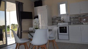 Een moderne keuken met witte kastjes, een ingebouwde oven en een eethoek met witte stoelen en een glazen tafel.