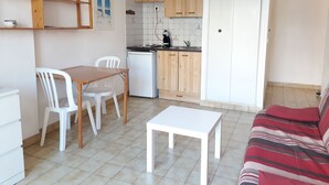 A compact living space with a kitchenette, a dining area with a table and chairs, and a sofa. - Studio Avec Clim et Parking Privėe (Cavalaire-sur-Mer)