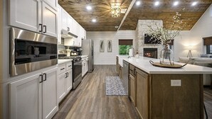 Une cuisine moderne avec des meubles blancs, des appareils en acier inoxydable, un plafond en bois et un îlot central agrémenté d’un vase.