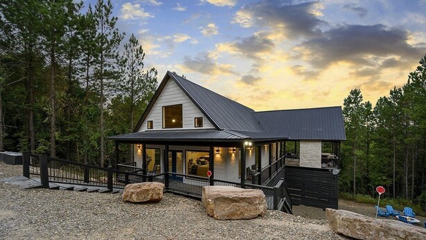 Un chalet moderne avec une façade en pierre, un porche abrité et un escalier menant à l’entrée.