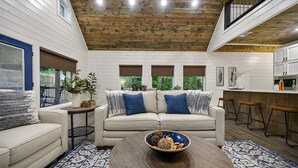 Un salon chaleureux avec un plafond en bois, un canapé beige agrémenté de coussins bleus, une table basse avec un bol décoratif et un tapis à motifs.