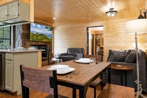 A wooden interior with a dining table set for two, a sofa, and a kitchen area with a stone wall and a large window. - Dolly's Castle unit 3 (Sevierville)