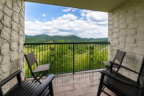 A balcony with two wicker chairs, a black metal railing, and a view of green hills under a partly cloudy sky. - Dolly's Castle unit 3 (Sevierville)