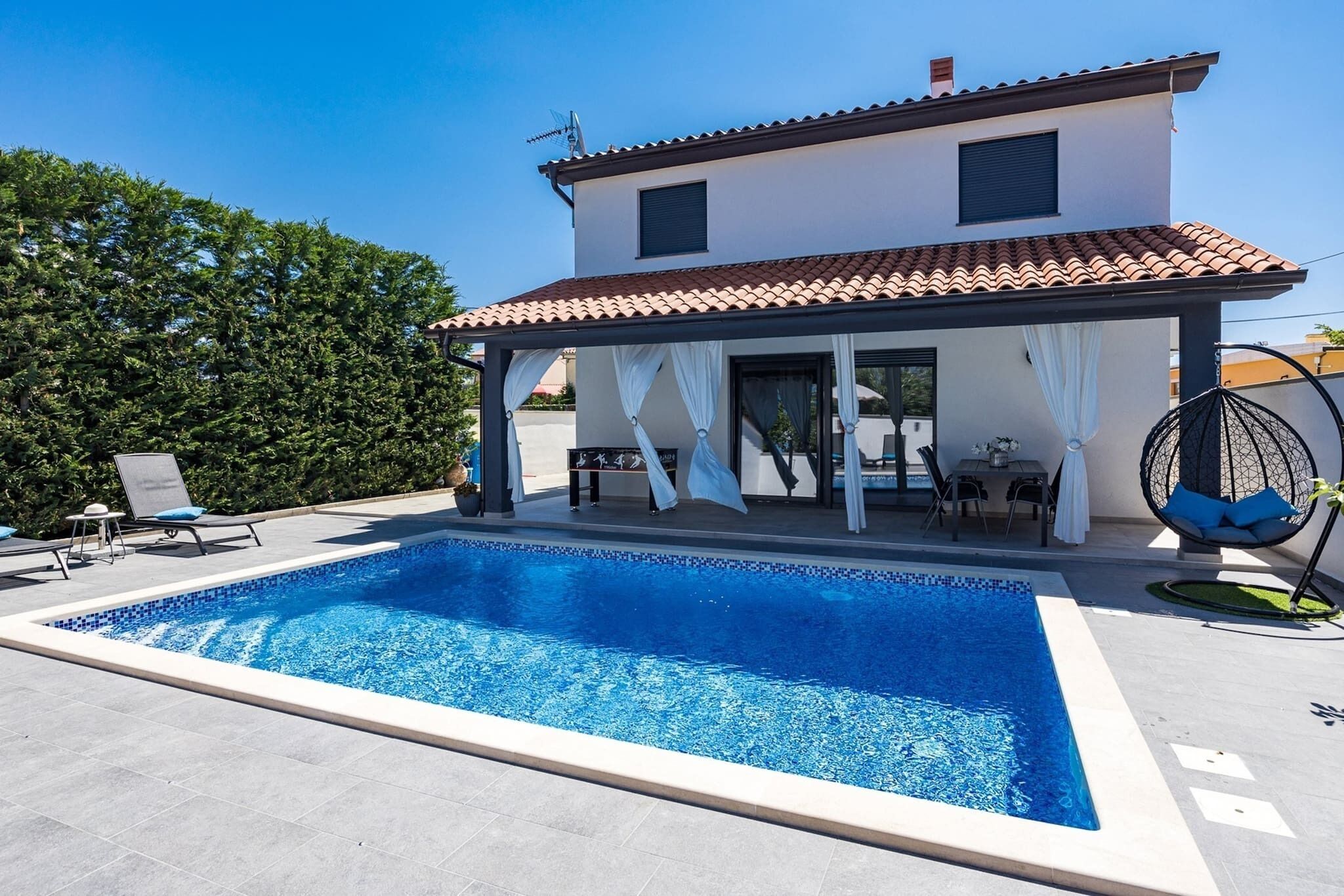 A two-story house with a swimming pool, outdoor seating, and a pergola.