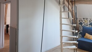 Ein Schlafzimmer im Loft-Stil mit Holzbalkendecke, einer Wendeltreppe, einem blauen Sofa und einem weißen Bett.