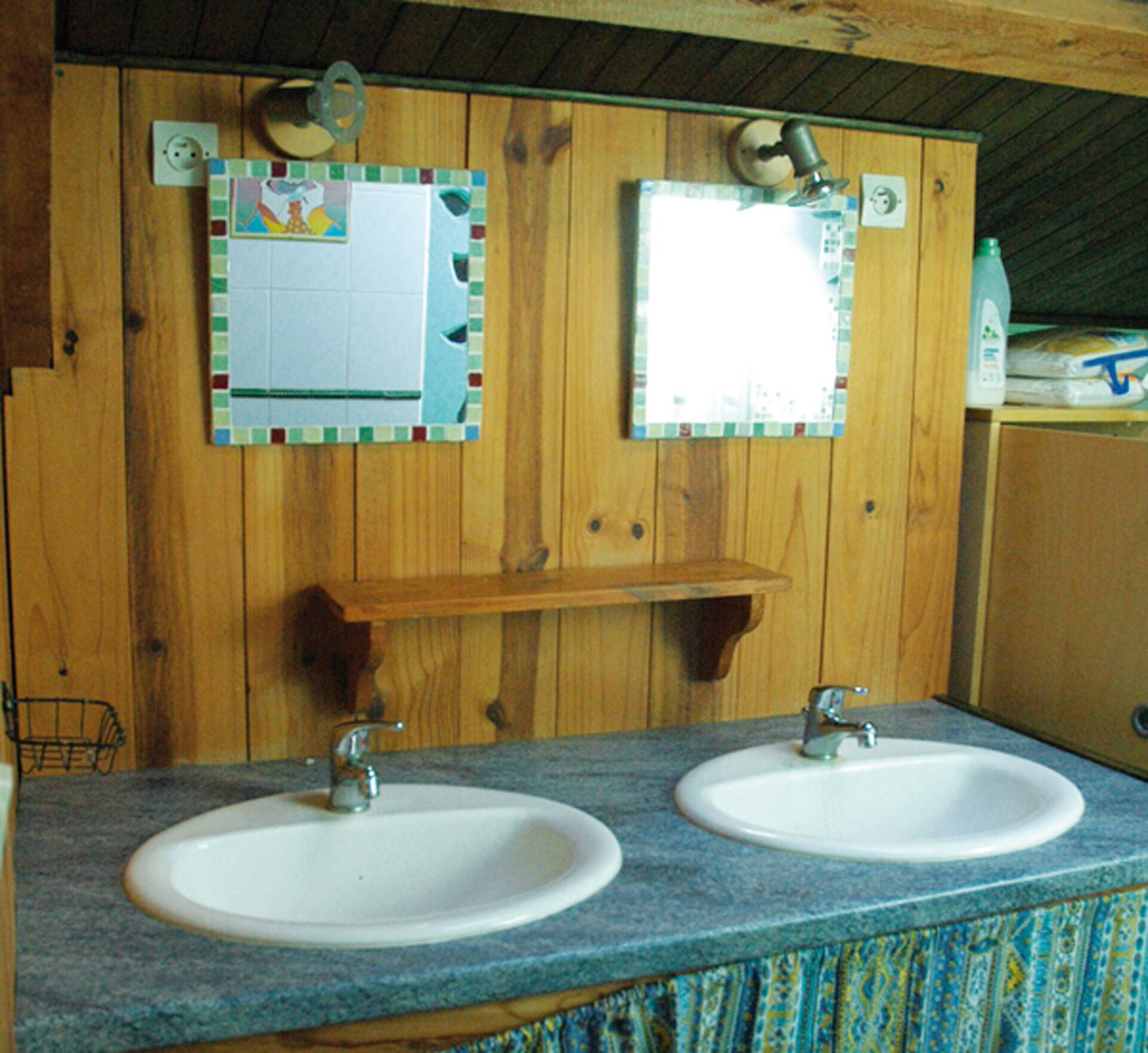 A bathroom with two sinks, wooden walls, and a mirror above each sink.