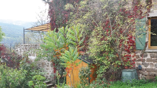 Ein Steinhäuschen mit Garten, Holzzaun und Metall-Pergola.