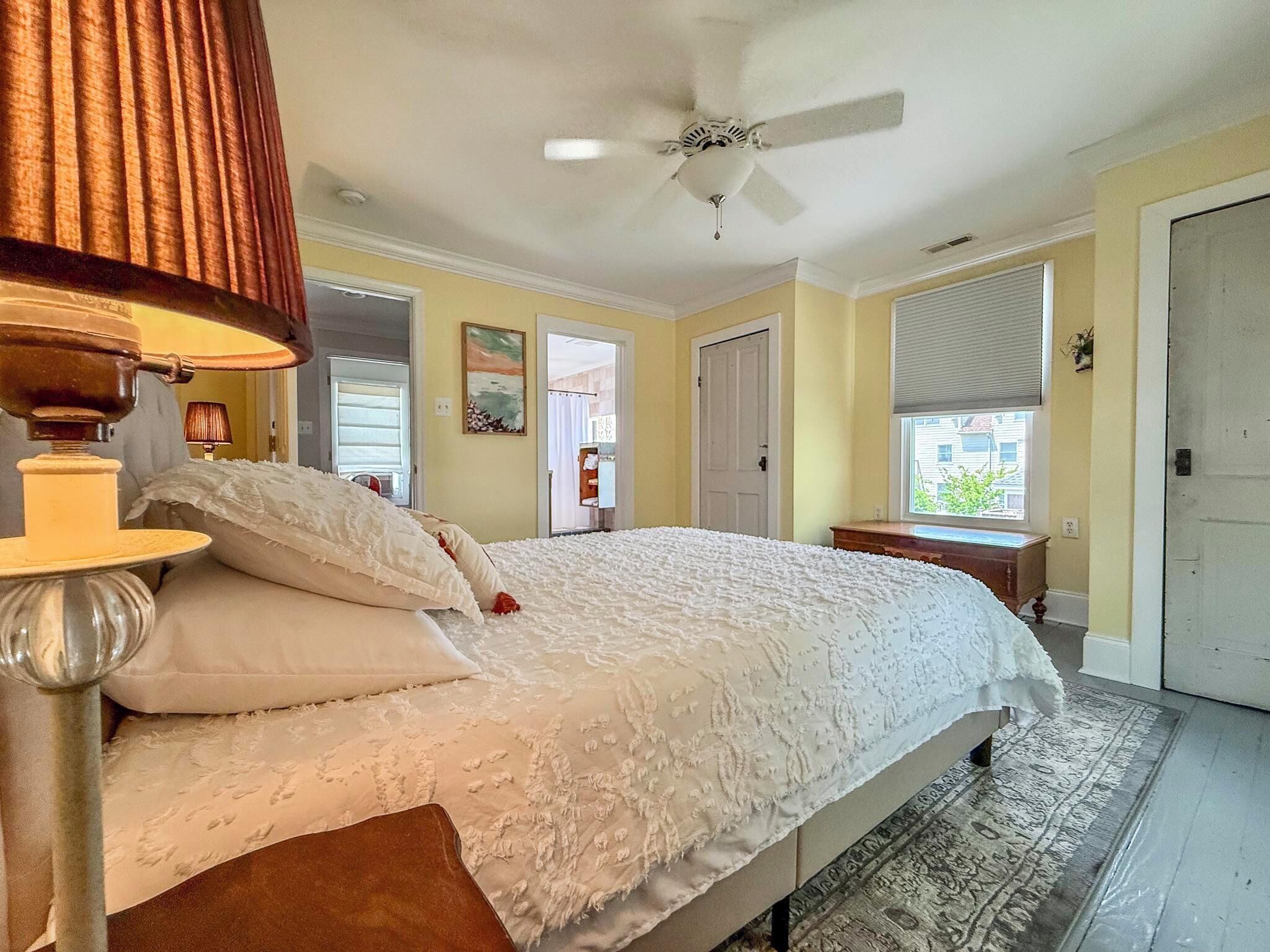 Un dormitorio con cama, ventilador de techo, lámpara y ventana con persianas.